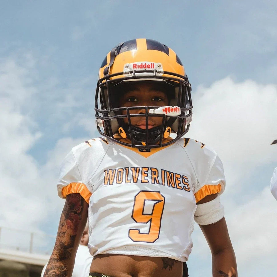 Young football player looking at camera, with a fangs mouthguard in his face mask 