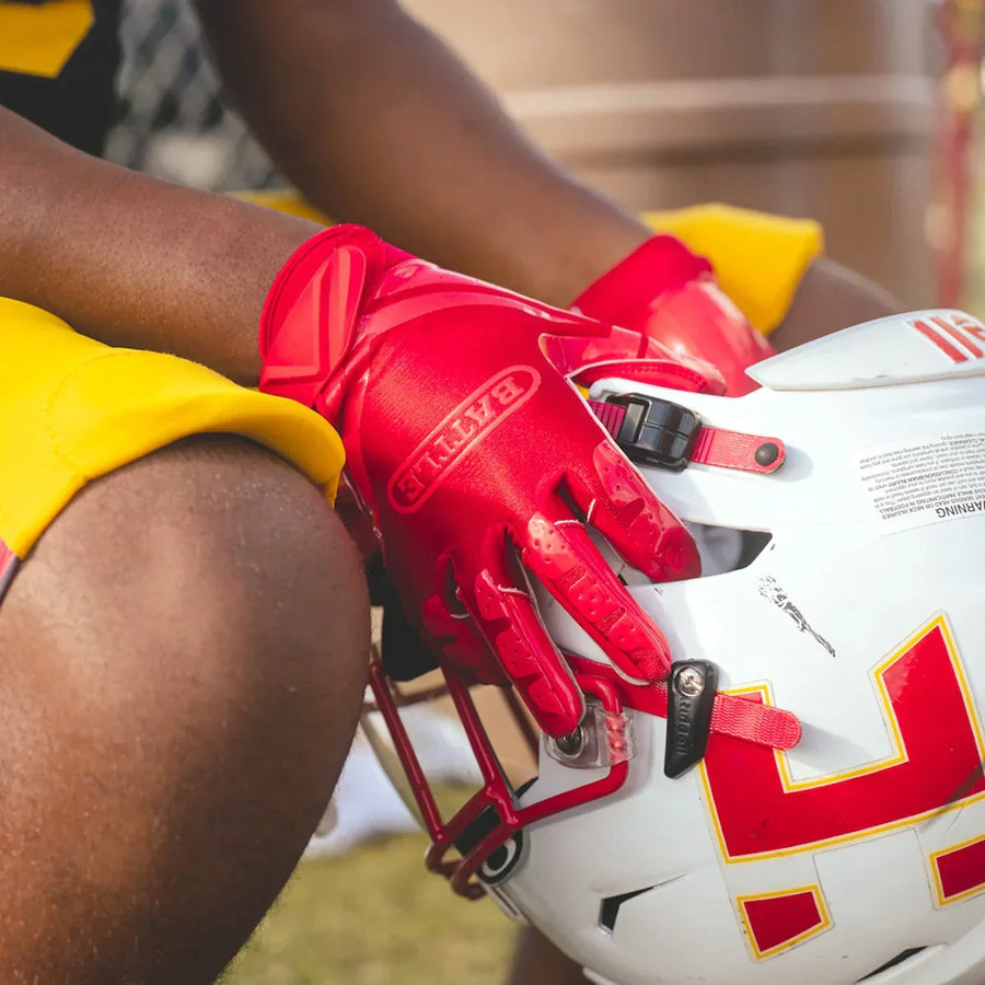 Football player wearing red Battle football gloves and holding his helmet