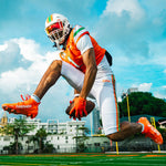 A pair of bright orange cleats with 'BATTLE' printed in white on the side, displayed against a clean white background.