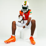 A pair of bright orange cleats with 'BATTLE' printed in white on the side, displayed against a clean white background.
