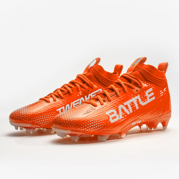 A pair of bright orange football cleats with white 'BATTLE', displayed on a clean white background.