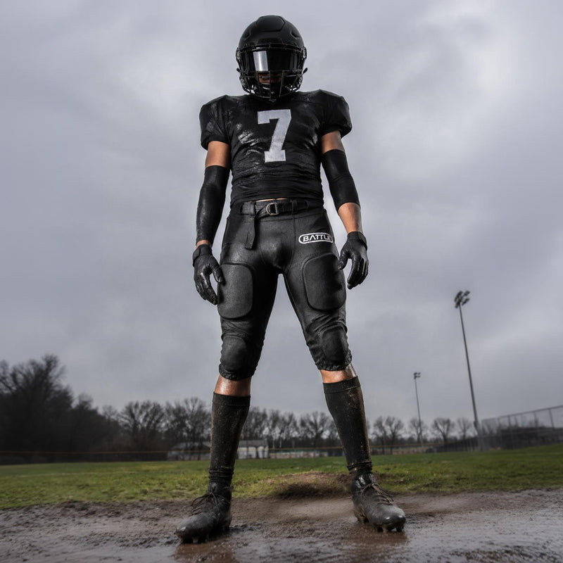 A football player stands in the mud on a rainy, overcast day.